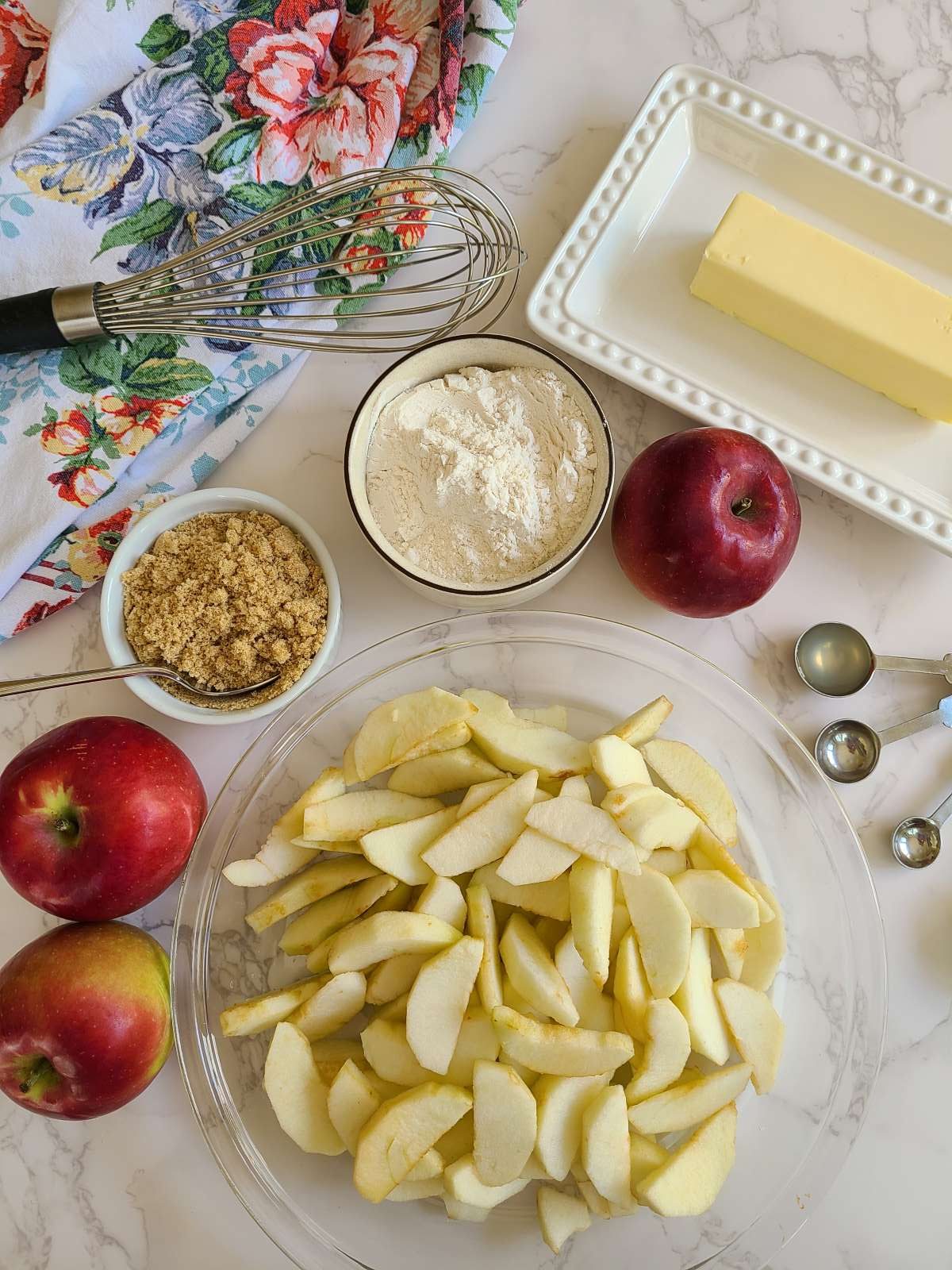 Ingredients for making apple betty, sliced apples, flour, butter, brown sugar and lemon juice.